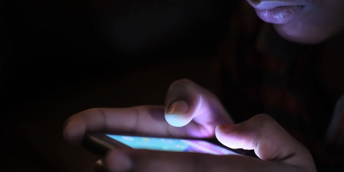 Mani che scorrono uno smartphone illuminato al buio